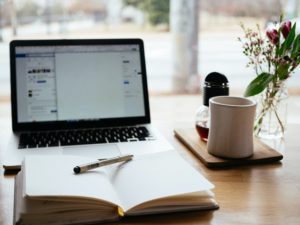 a wooden desk with flowers, a mug, a laptop, and a notebook open for taking notes on self-employed mortgages