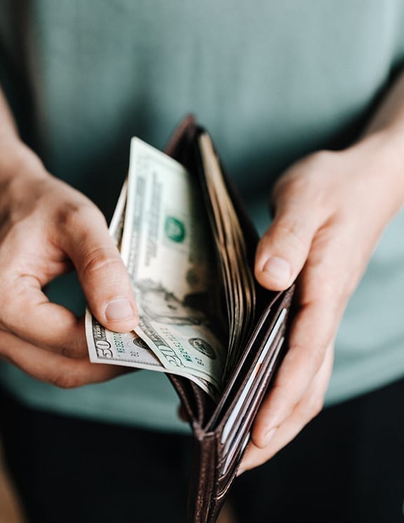 Closeup of hands holding a wallet and pulling out dollar bills, in reference to a mortgage down payment