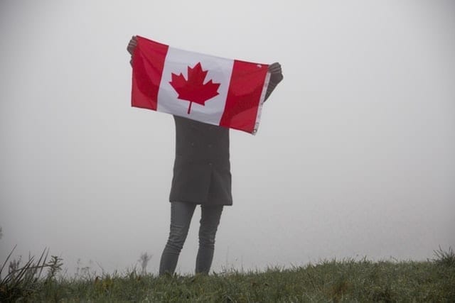 A woman holding up a Canadian flag outdoors on a foggy day; highlighting the New to Canada Mortgage program