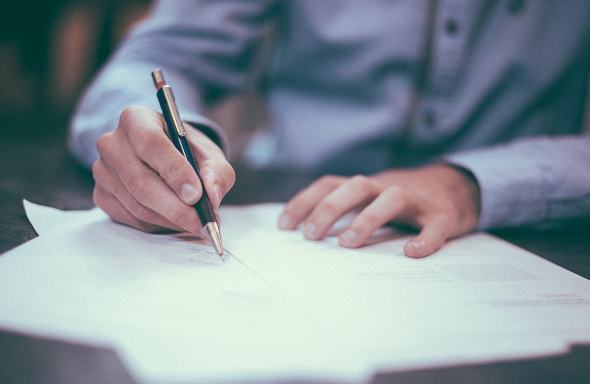 Man in blue shirt closeup of hands signing paperwork; mortgage vendor take-back usually offers less paperwork