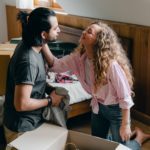 A couple looking adoringly at each other, surrounded by moving boxes after a real estate purchase