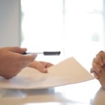 closeup of hand holding a pen and paper, in a gesture to hand this off to another person; highlighting securing a mortgage post covid 19