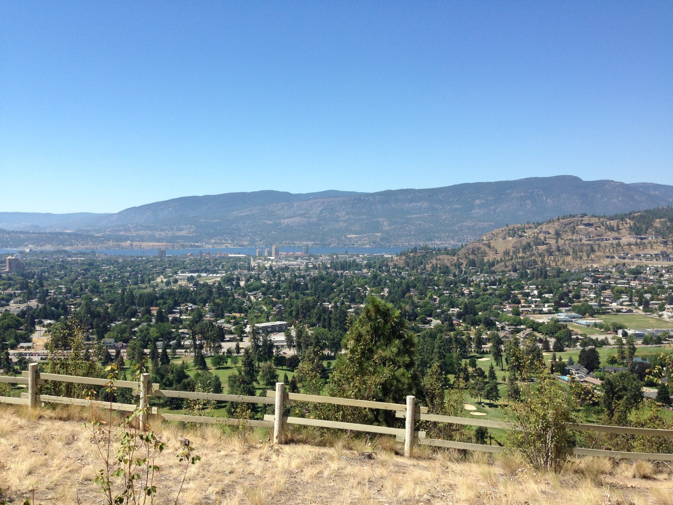 Valley view of residential Kelowna on a clear sunny day, with mountains and Okanagan lake in background