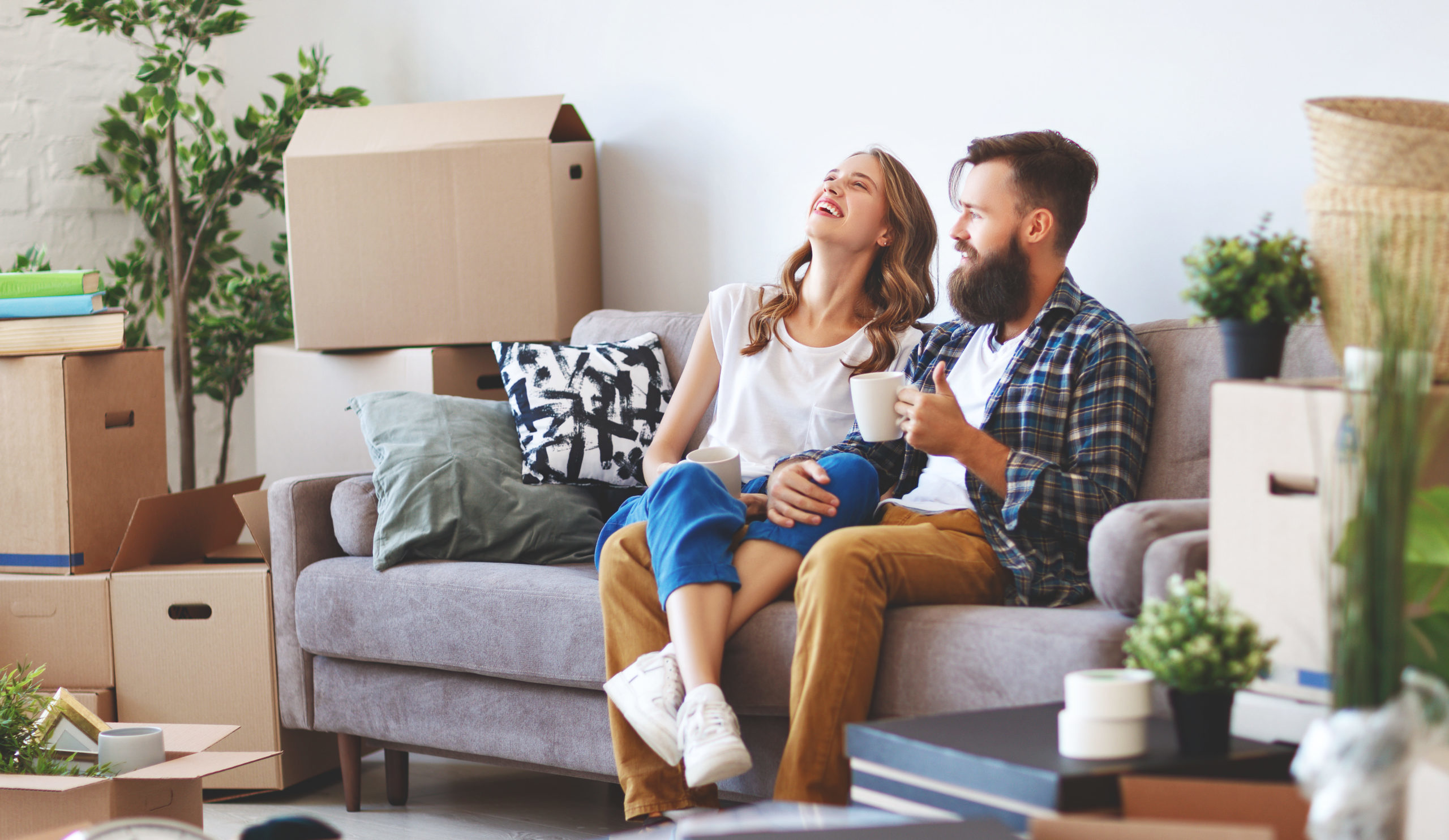 A happy young couple laughing on the couch in their first home surrounded by moving boxes