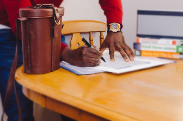 man signing a document related to amortization for mortgages on a wooden kitchen table with a brown leather satchel on the table