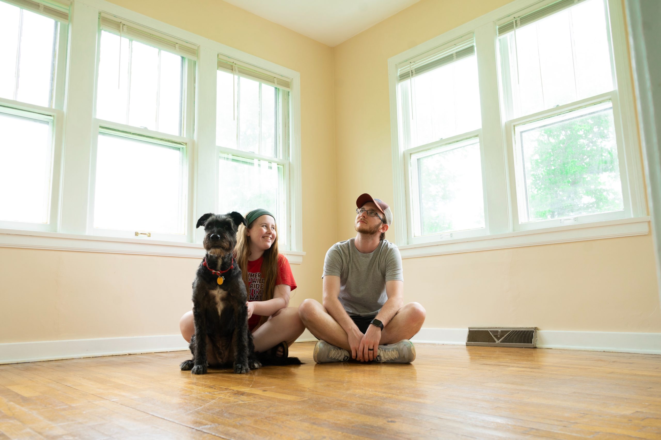 A young couple and their dog sitting on the floor in an empty room in their new house