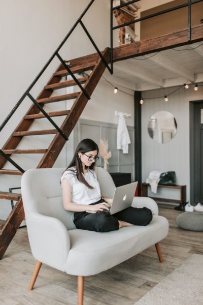 a first time home buyer sitting on a couch in a loft apartment on her computer