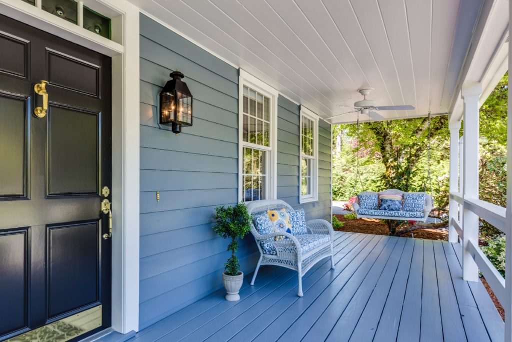 the front porch of a house with a black door and blue siding, a house purchased with subjects