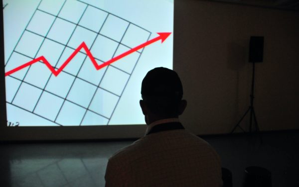 A silhouette of a man looking at a projector screen with a graph of mortgage rate hikes with a red arrow going up