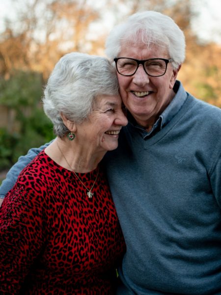 Senior couple standing side by side and the man has his arm around the woman; relating to being 55+ to qualify for a reverse mortgage. 