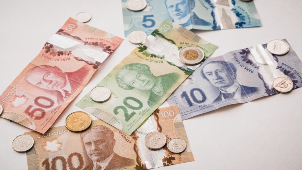 canadian dollar bills and coins on a white surface, in reference to the money you'll save from paying off your mortgage early