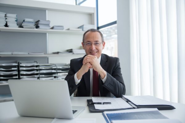 real estate lawyer sitting a desk with hands together in front, smiling and looking at camera